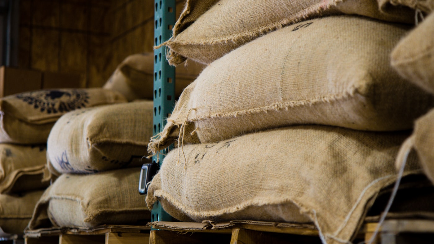 Burlap sacks of green coffee beans stacked on warehouse racks